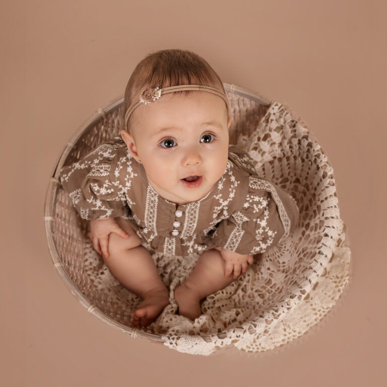 Schattig klein meisje tijd in een witte rieten mand tijdens een sittershoot
